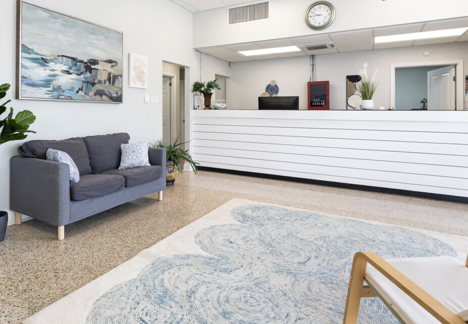 A living room with a couch , chair , rug and a clock on the wall.