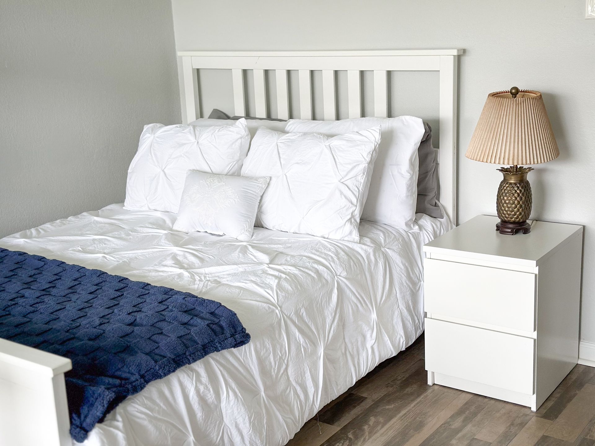 A bedroom with a bed , nightstand , lamp and blue blanket.
