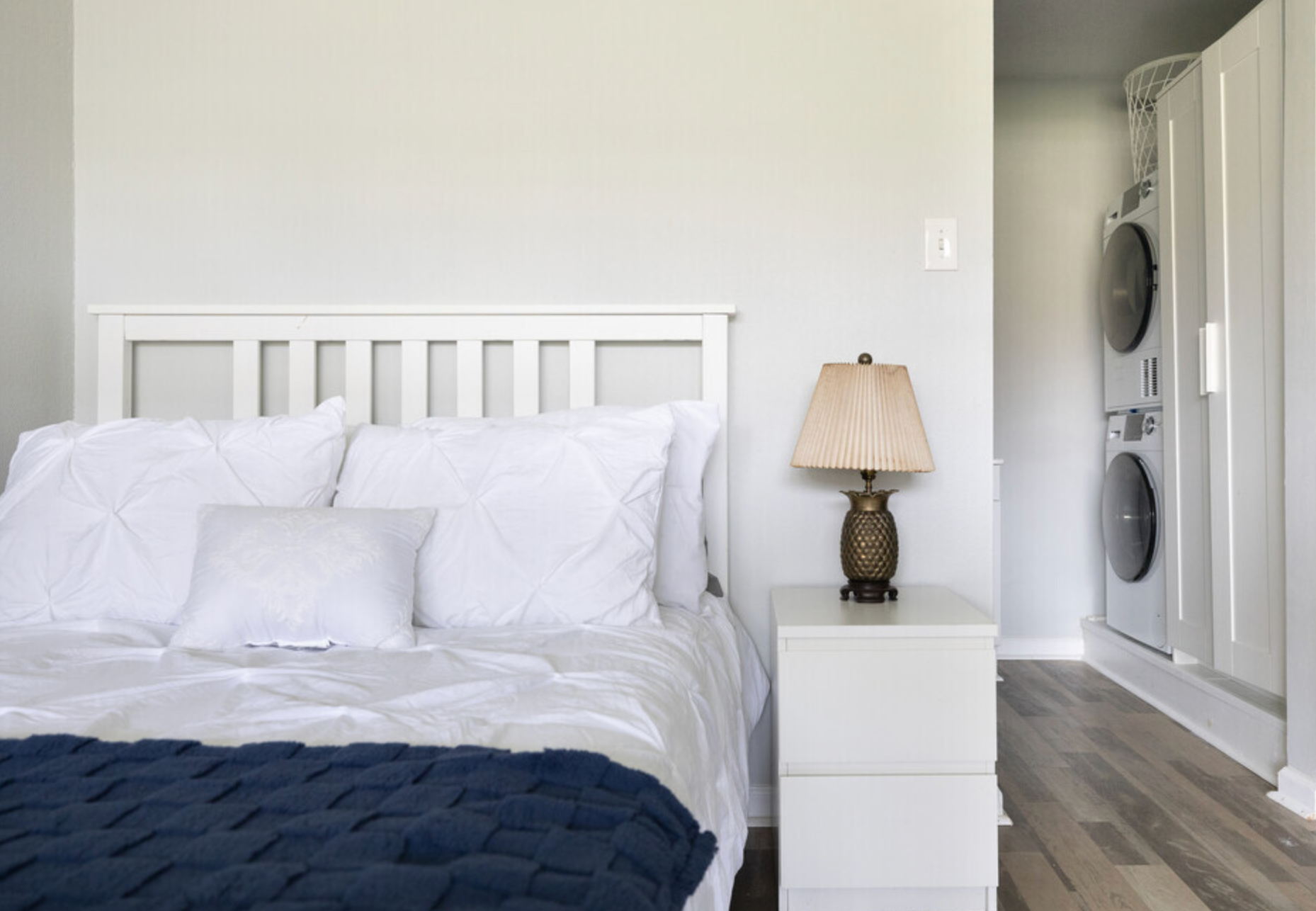A bedroom with a bed , nightstand , lamp and washer and dryer.