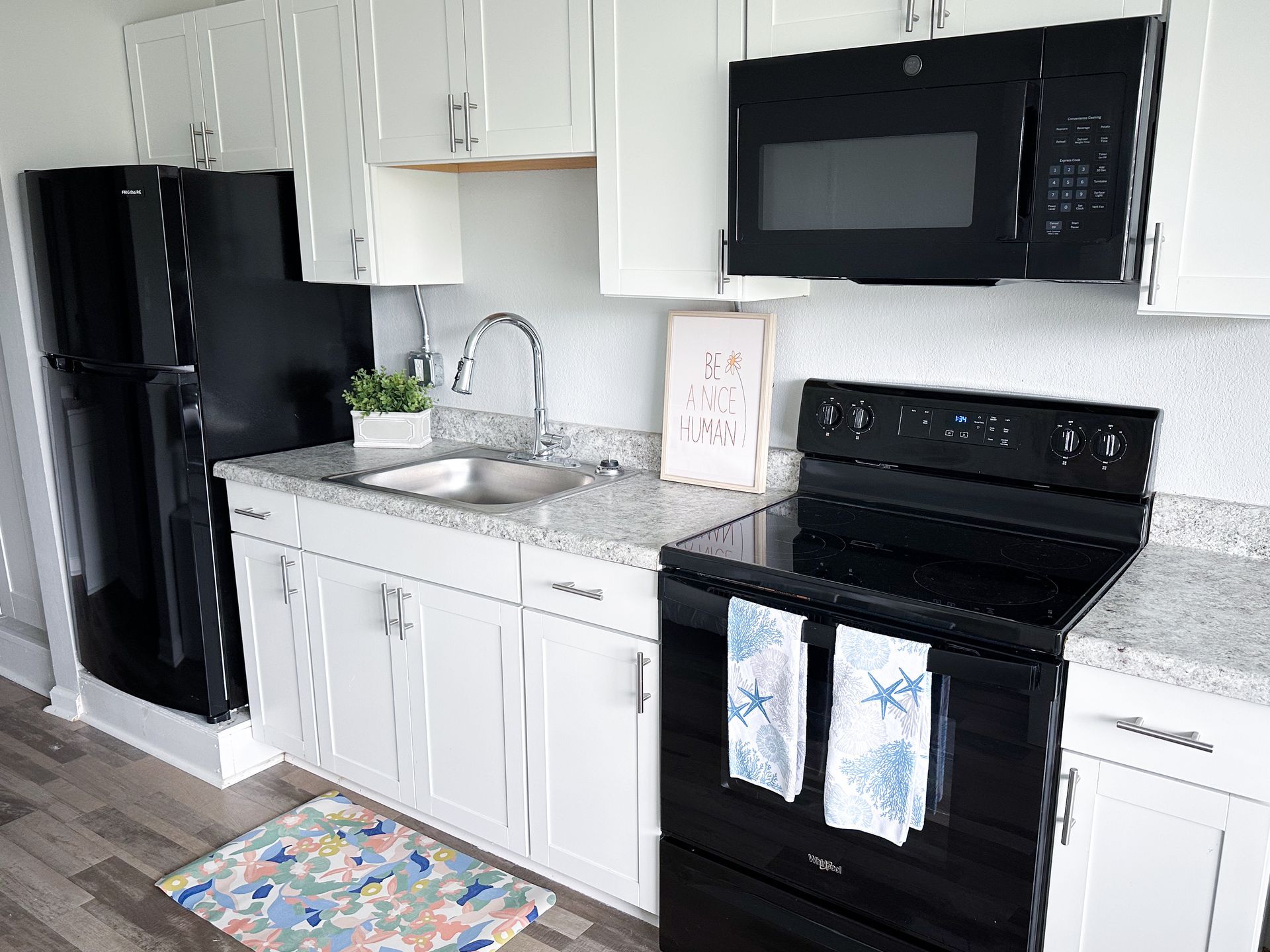 A kitchen with white cabinets , a black refrigerator , a black stove , and a black microwave.
