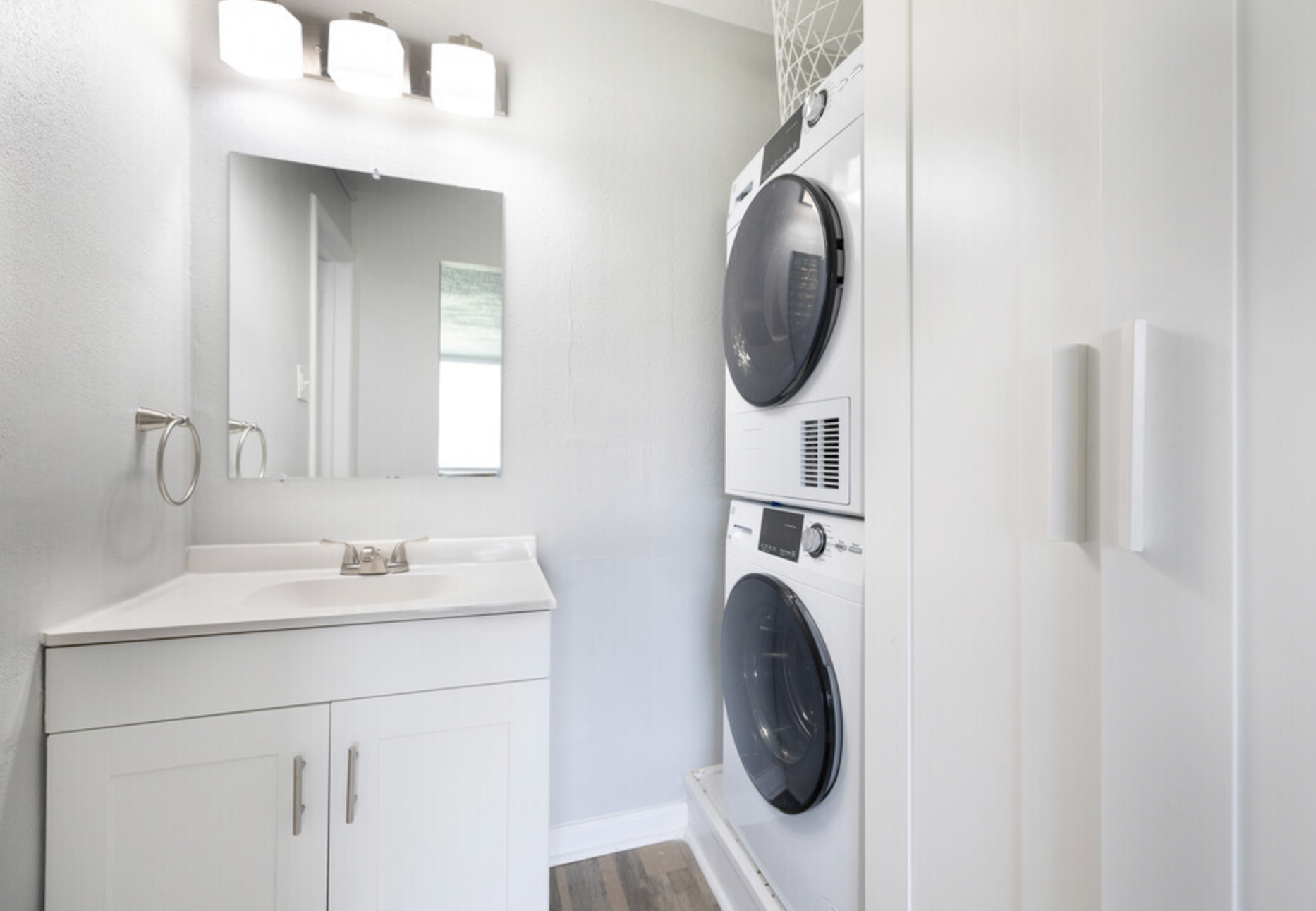 A bathroom with a sink , washer and dryer stacked on top of each other.