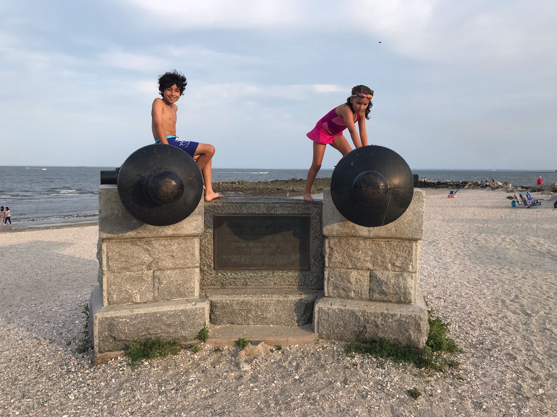 A boy and a girl are standing on top of a statue on the beach.
