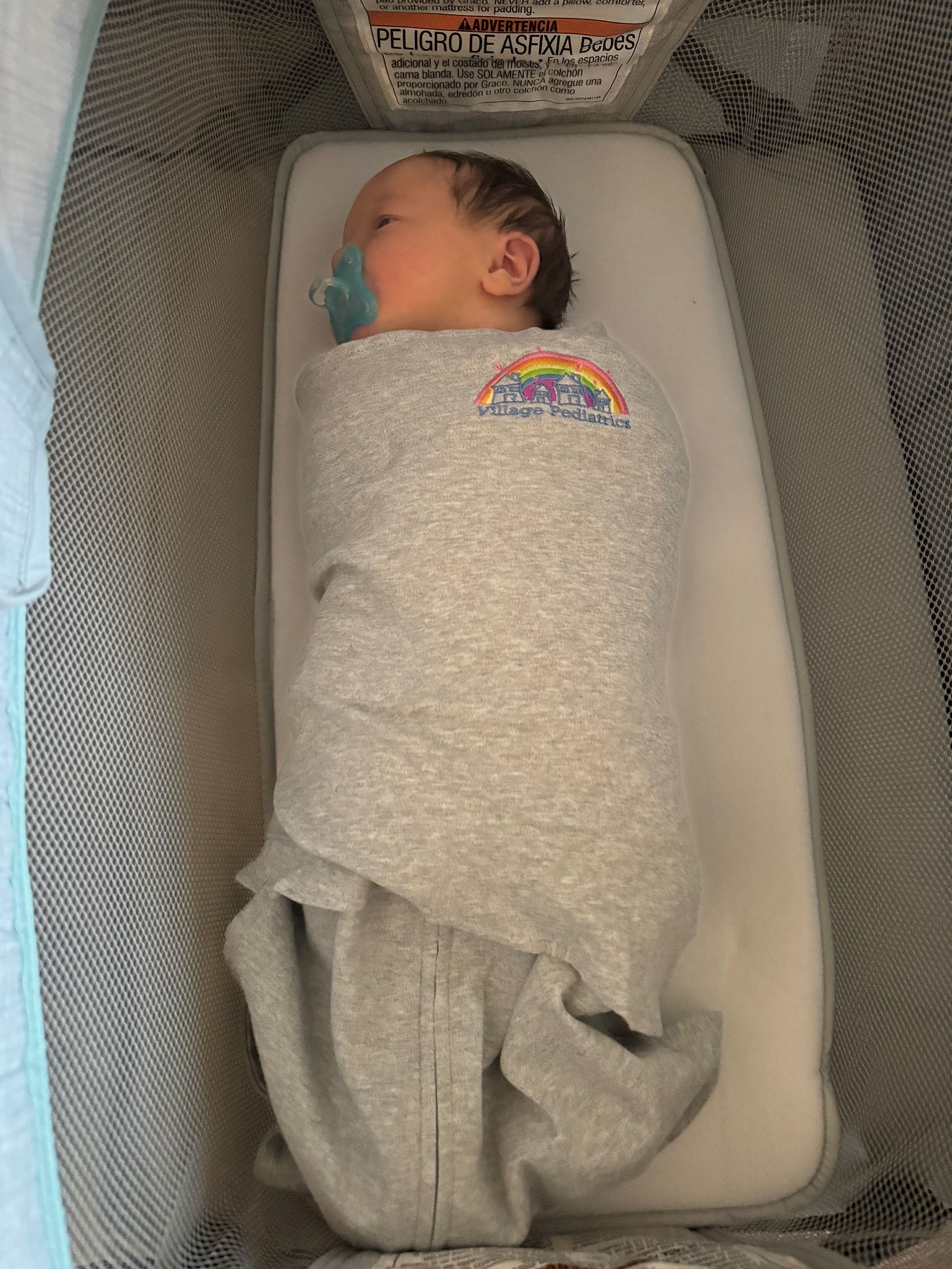 A baby is wrapped in a blanket and sleeping in a crib.