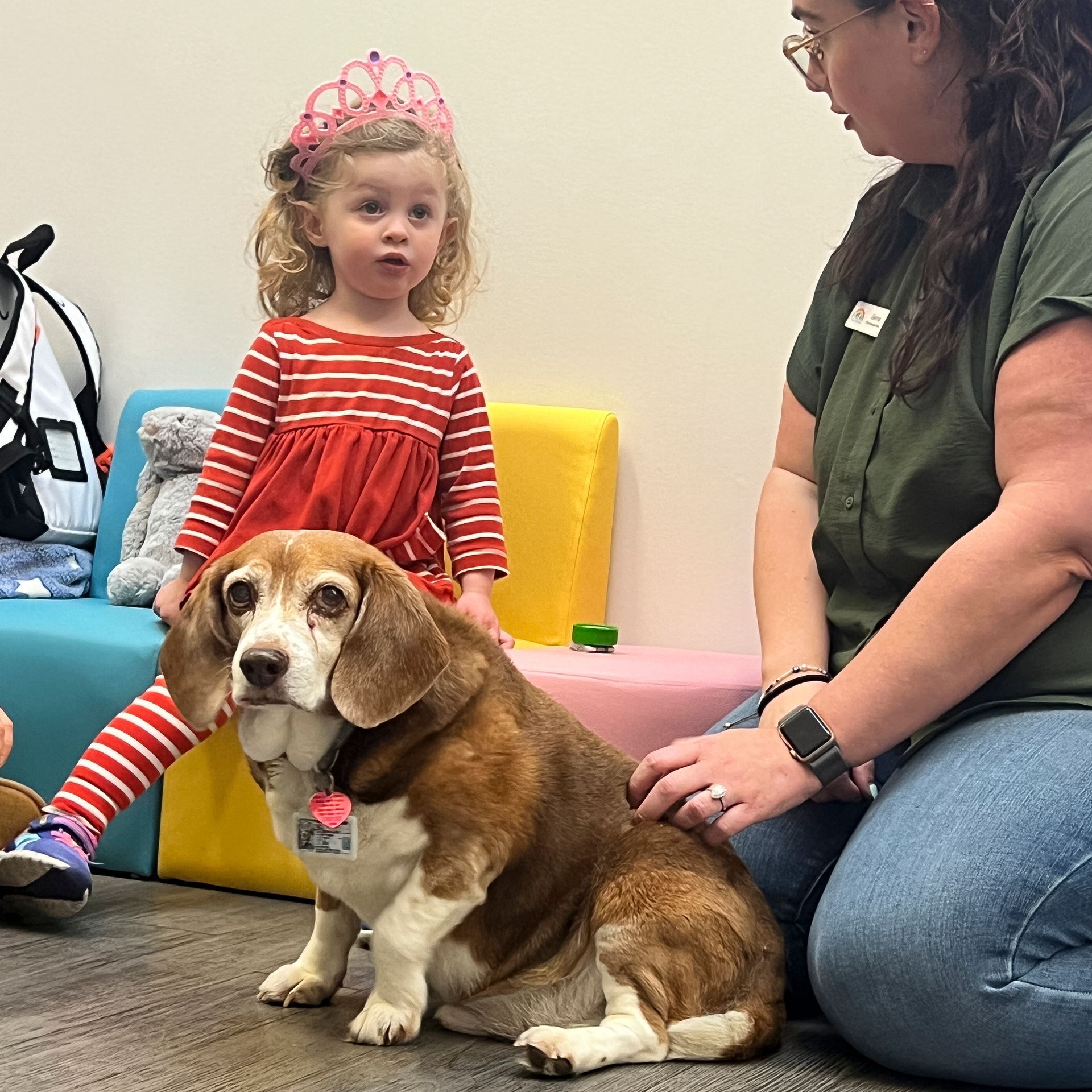 A little girl wearing a crown is sitting next to a dog.
