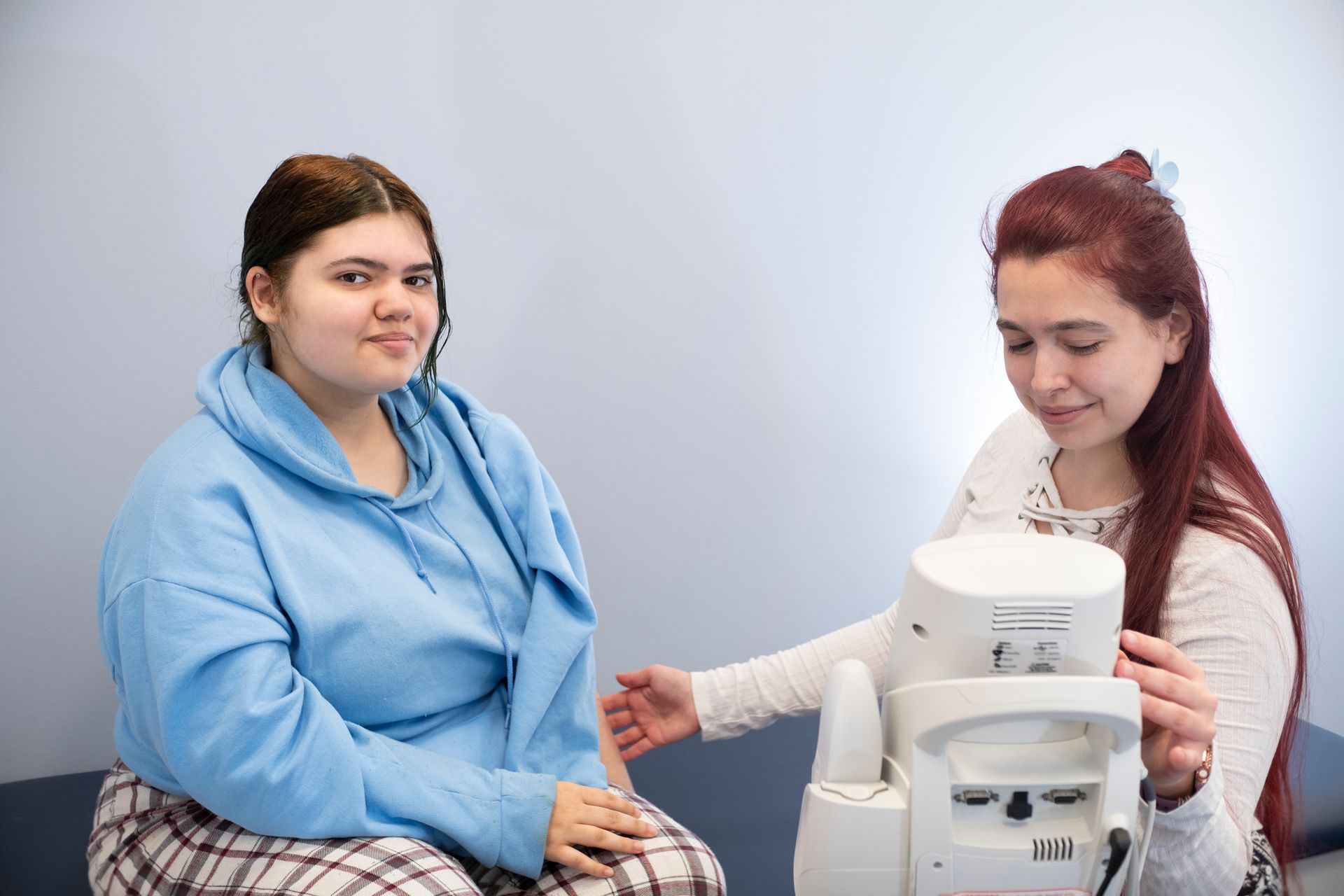 Two women are sitting next to each other in front of a coffee maker.