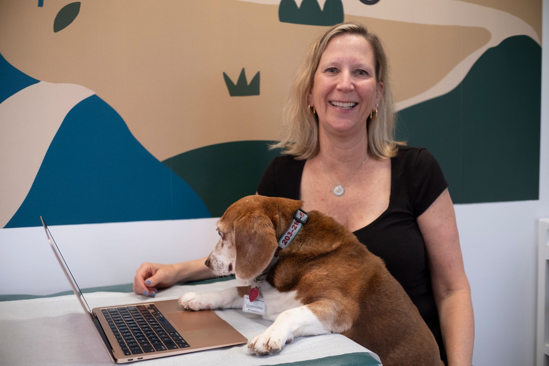 A woman is sitting at a desk with a dog on her lap.