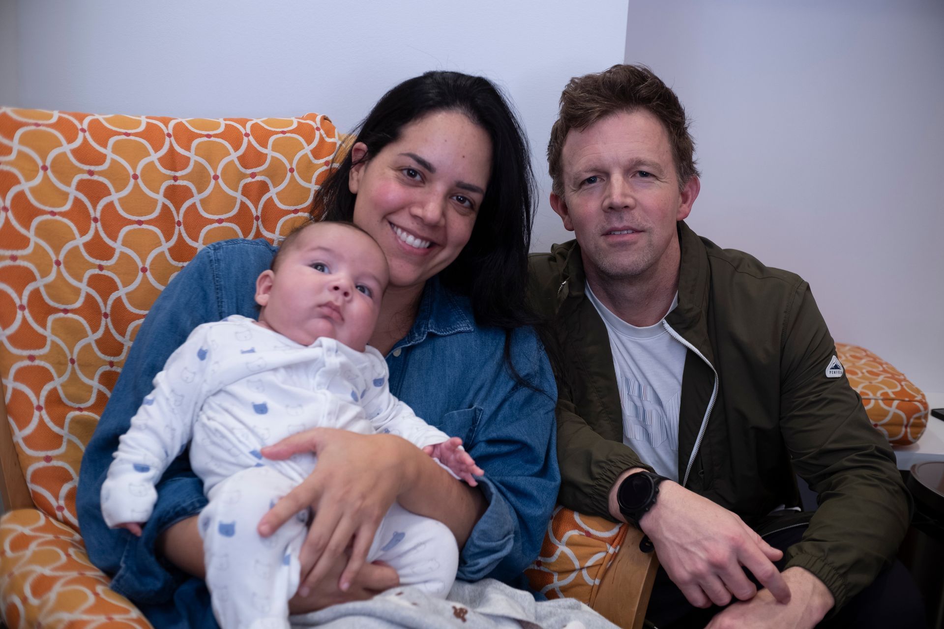 A man and a woman are sitting on a couch holding a baby.