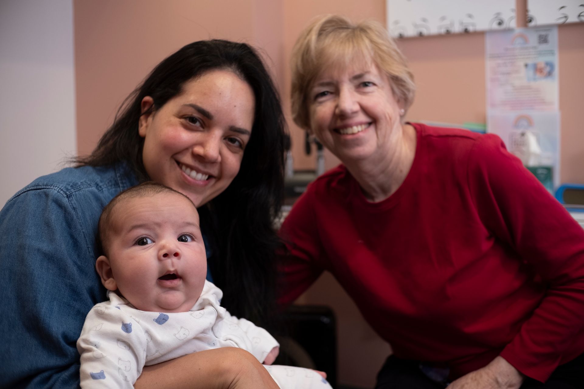 Two women are holding a baby and smiling for the camera.