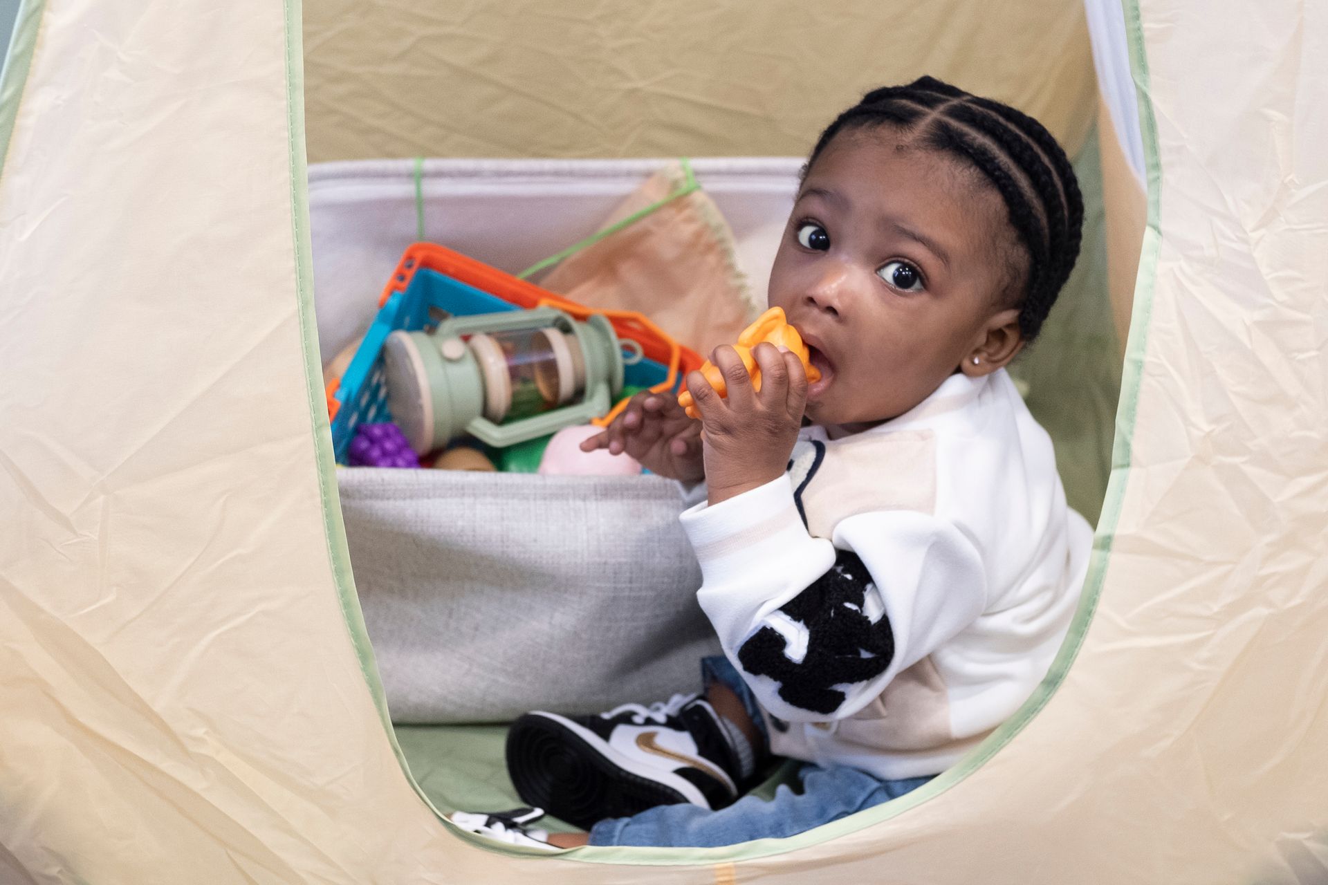 A baby is sitting in a tent eating a carrot