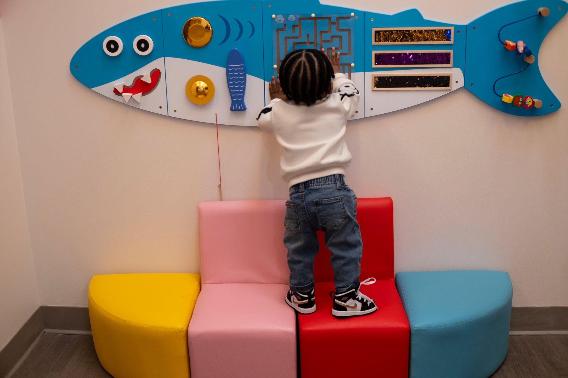 A little boy is standing on a chair in front of a fish shaped wall.