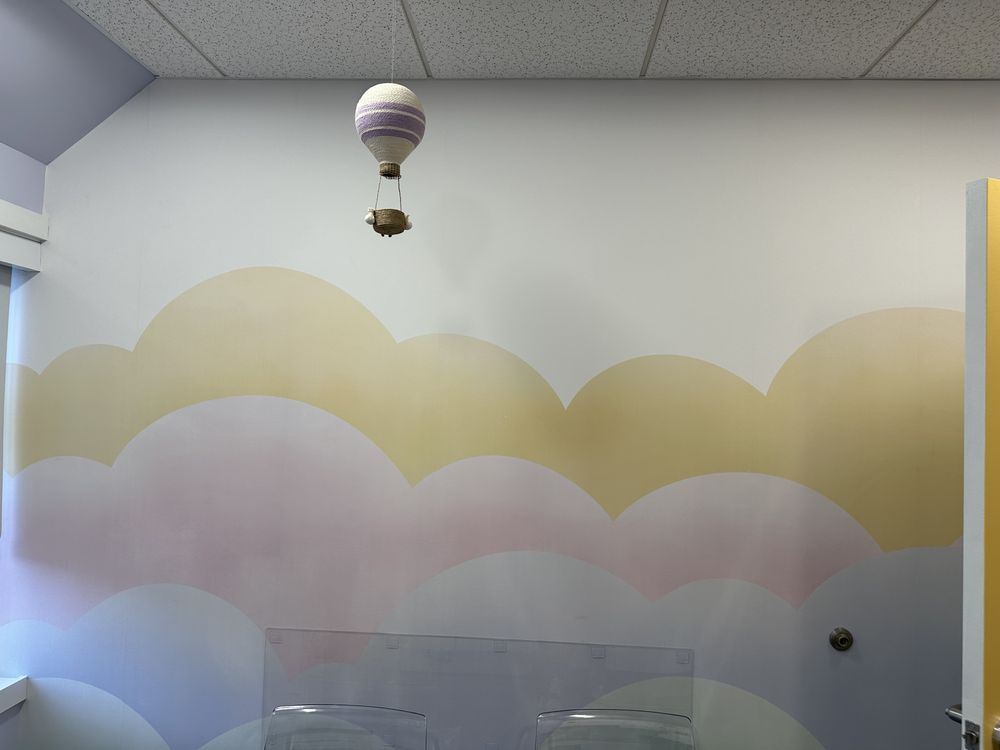 A hot air balloon is hanging from the ceiling in a room with clouds painted on the wall.