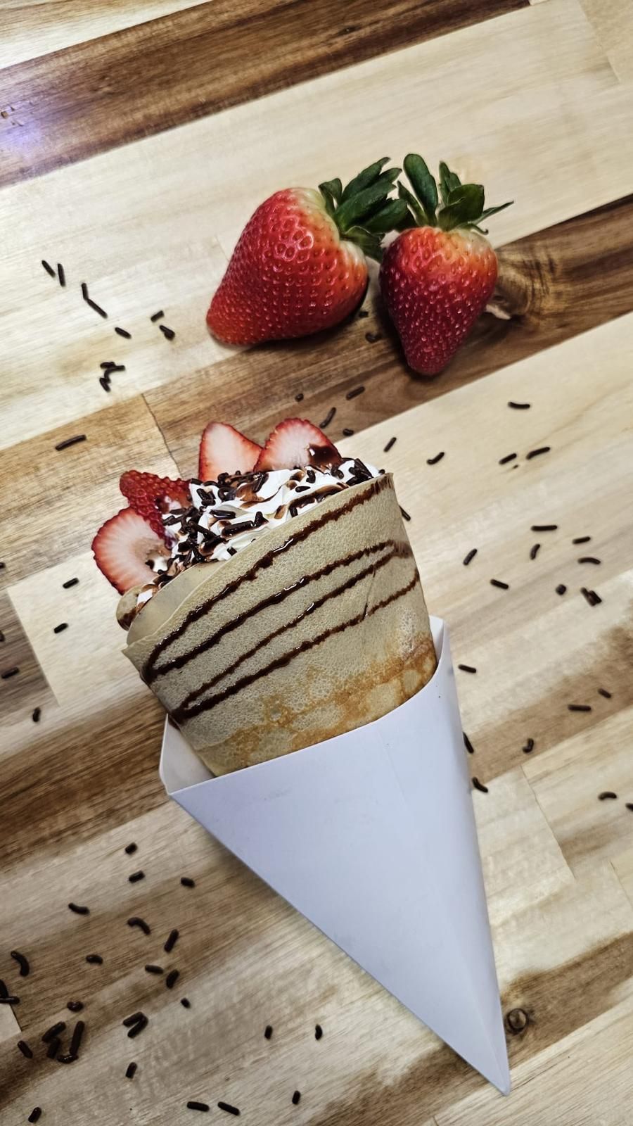 Crepe cone with strawberries, whipped cream, chocolate drizzle, and sprinkles.