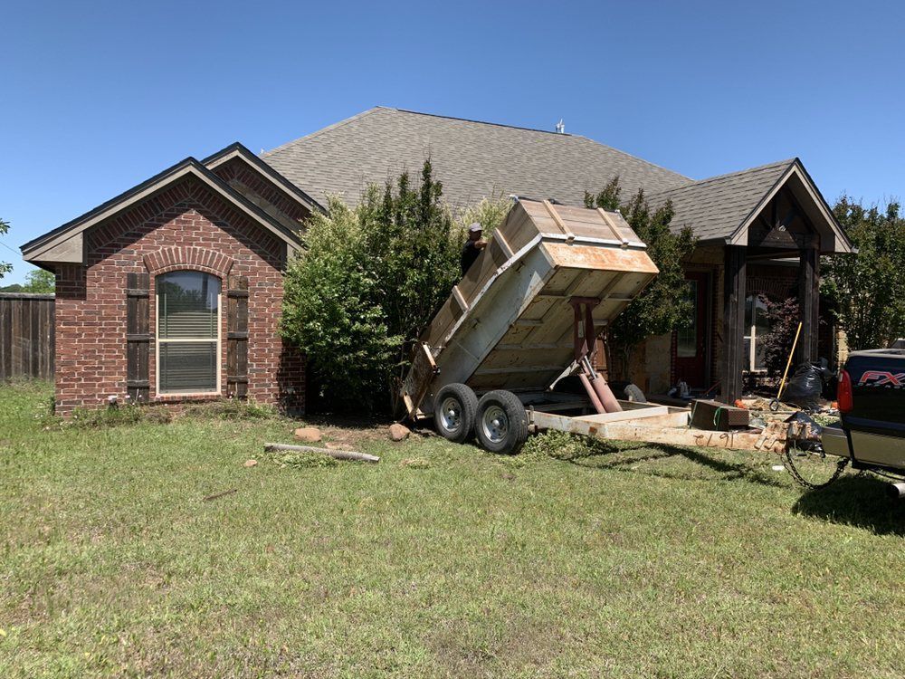 A dumpster is parked in front of a brick house.
