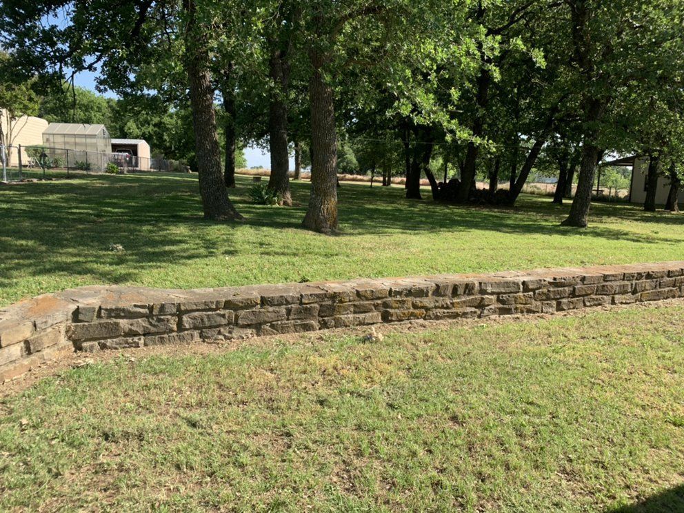 A stone wall in the middle of a grassy field with trees in the background.
