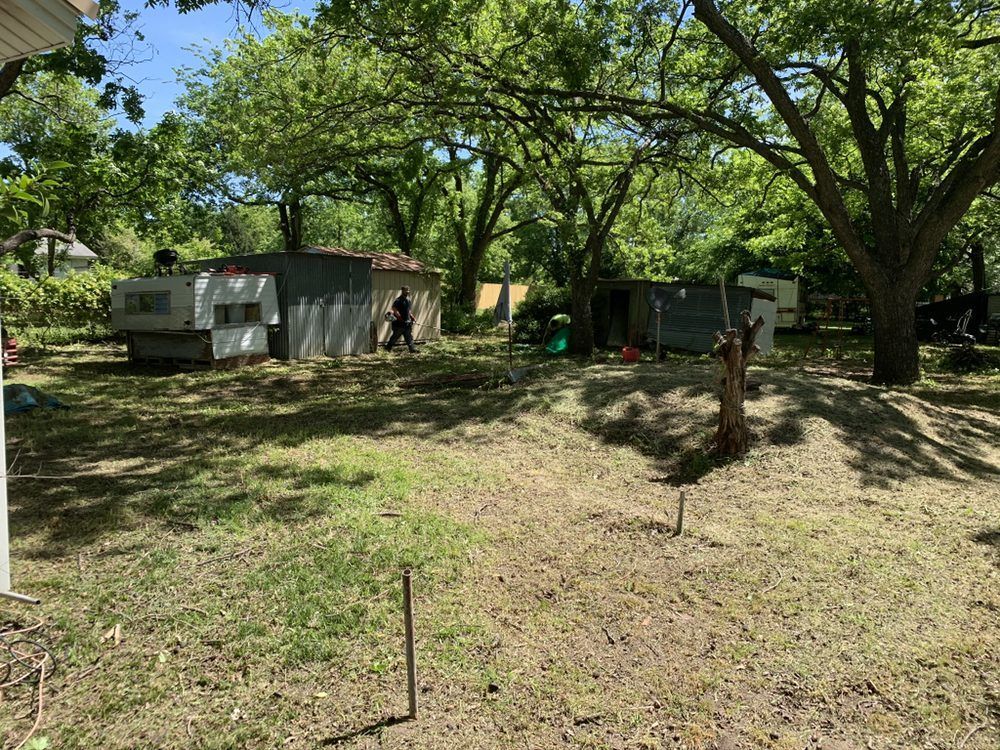 A yard with a trailer and a house in the background.