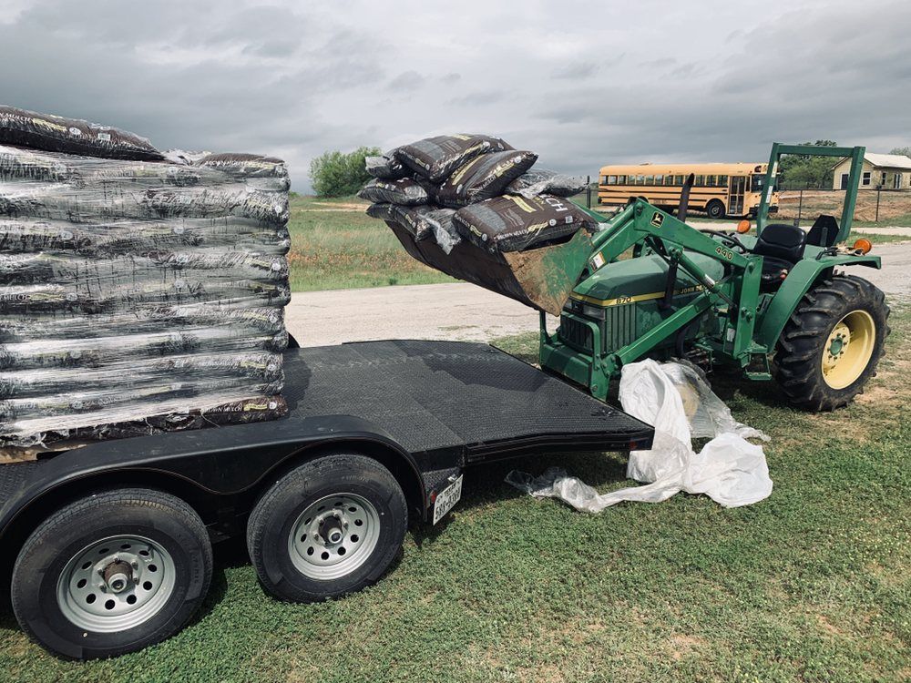 A green tractor is loading bags onto a trailer.