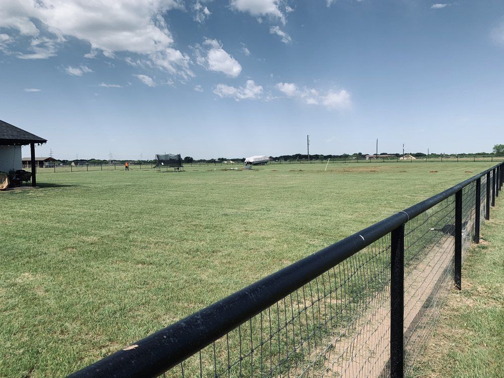 A black fence surrounds a large grassy field.