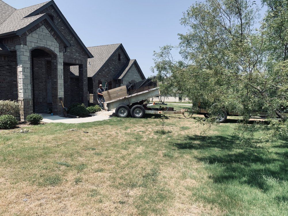A man is loading a dumpster into a trailer in front of a house.