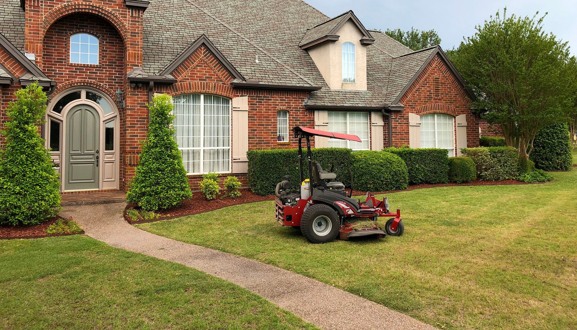 A lawn mower is parked in front of a large brick house.