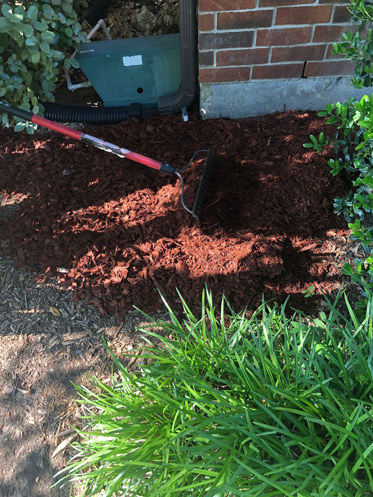 A shovel is sitting on top of a pile of mulch next to a brick wall.
