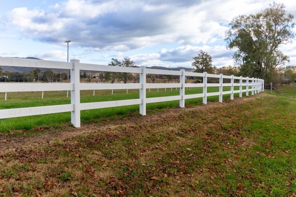 A White Fence Surrounds a Grassy Field With Trees in the Background — Turf Central In Airlie Beach, QLD