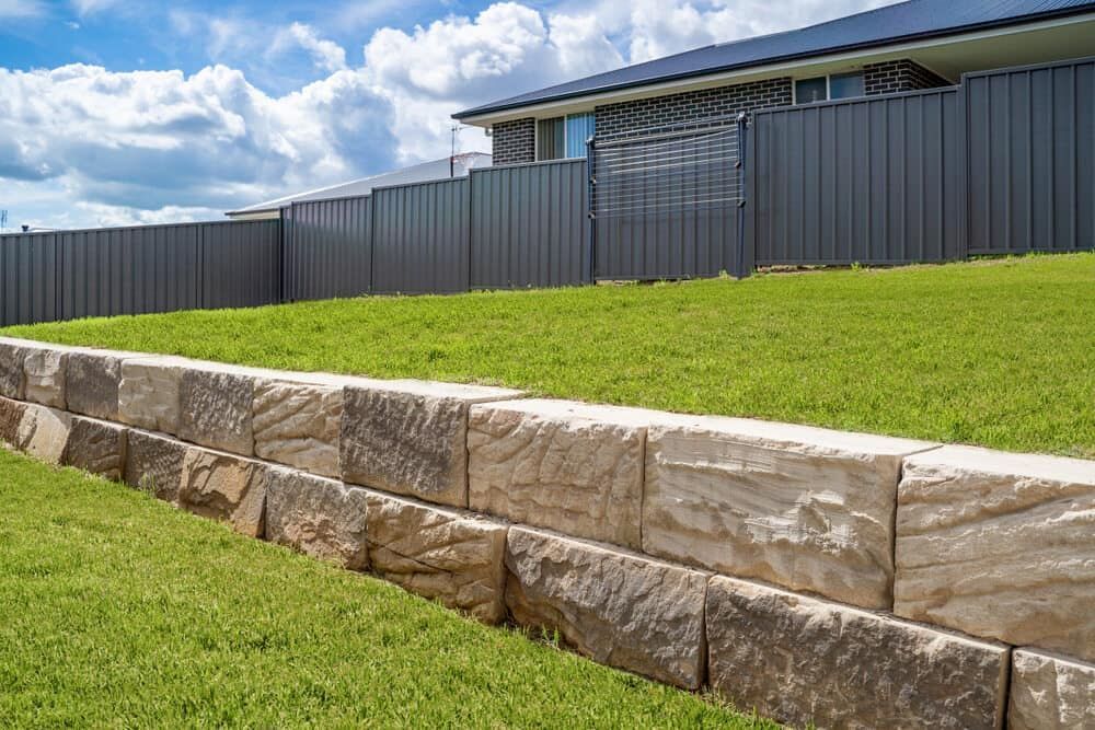 A Stone Wall Surrounds a Lush Green Lawn in Front of a House — Turf Central In Airlie Beach, QLD