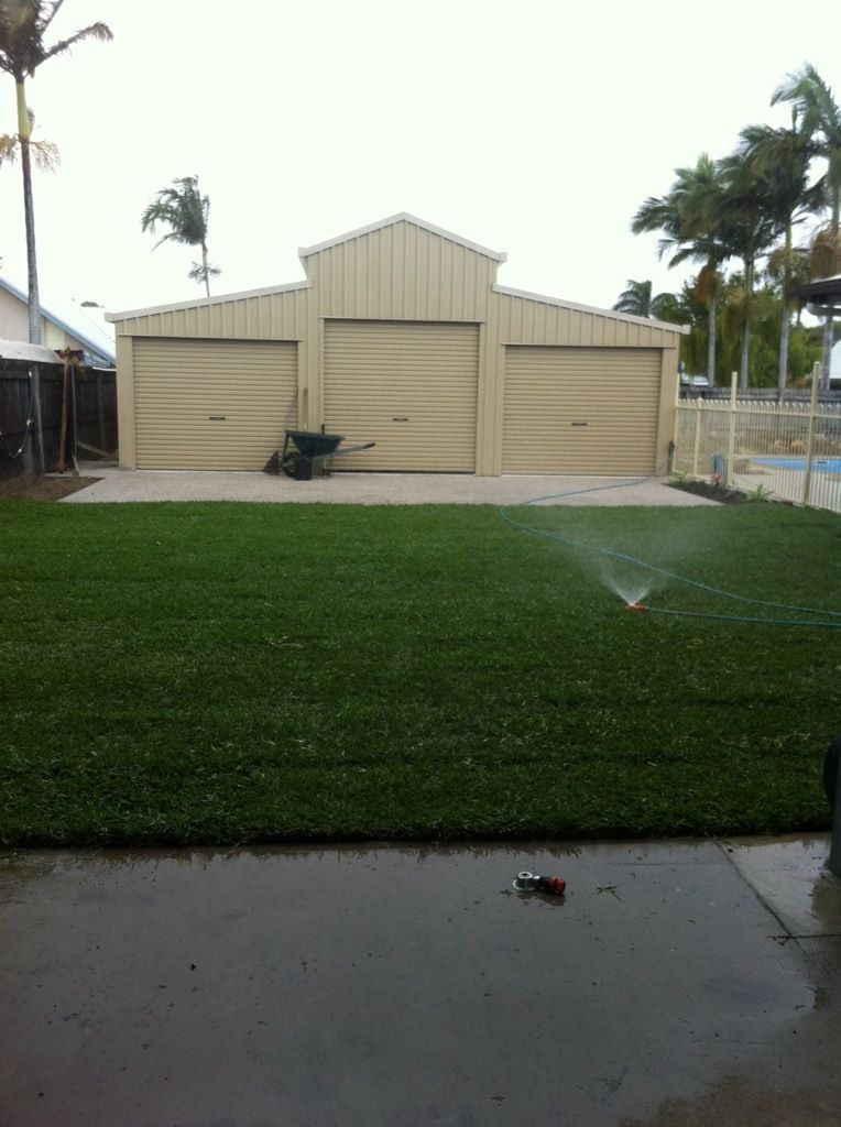 A Sprinkler is Spraying Water on a Lush Green Lawn in Front of a Garage — Turf Central In Chelona, QLD