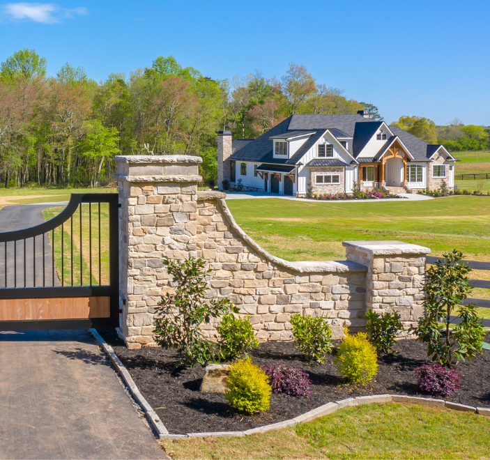 A large house is behind a stone wall with a gate