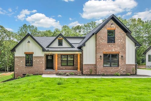 A large brick house with a black roof is sitting on top of a lush green field.