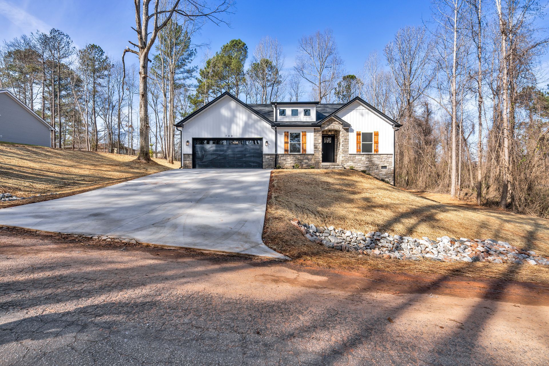 A white house with a black garage door is surrounded by trees and a driveway.