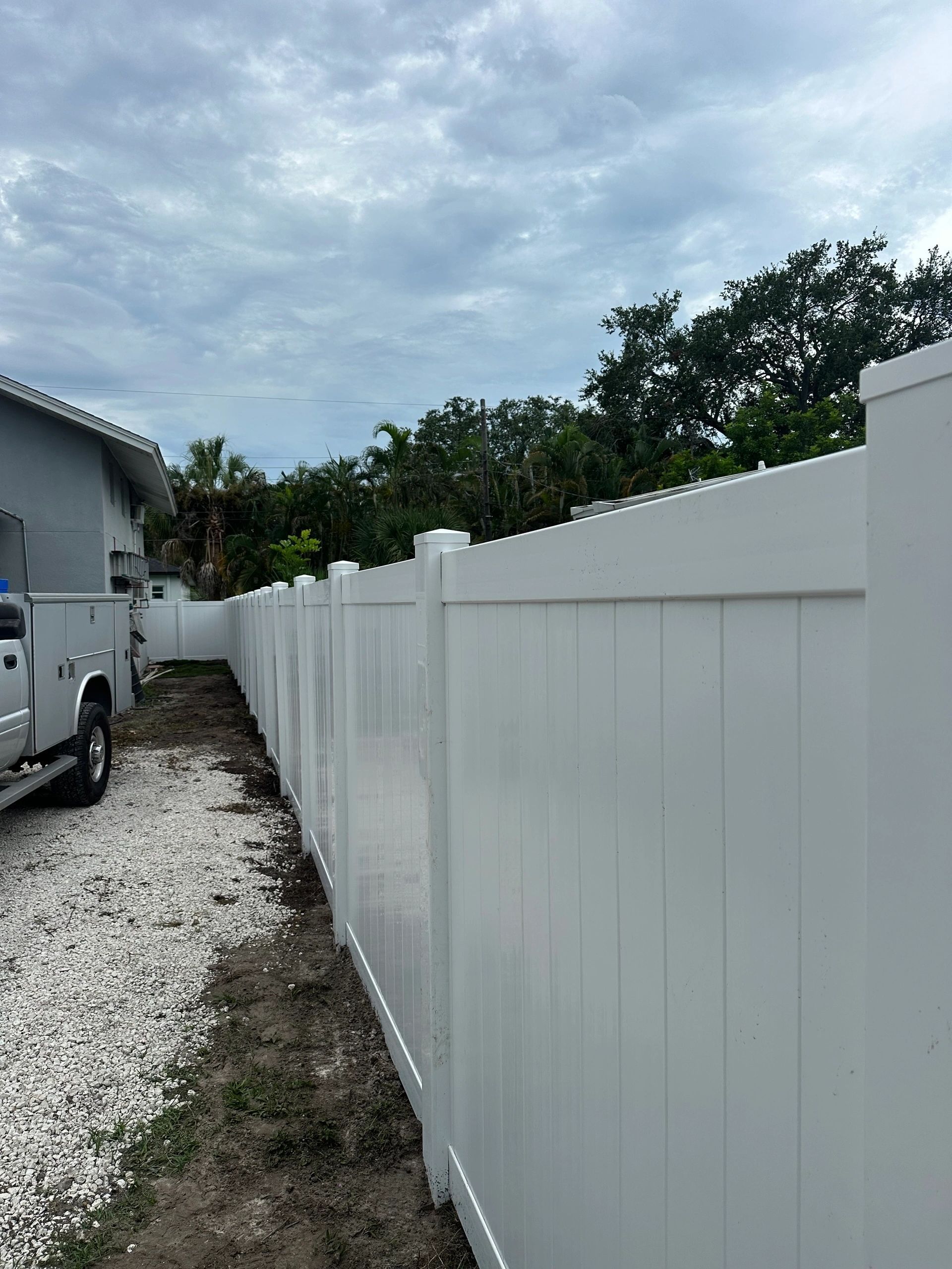 A white pick up truck is parked next to a white fence.