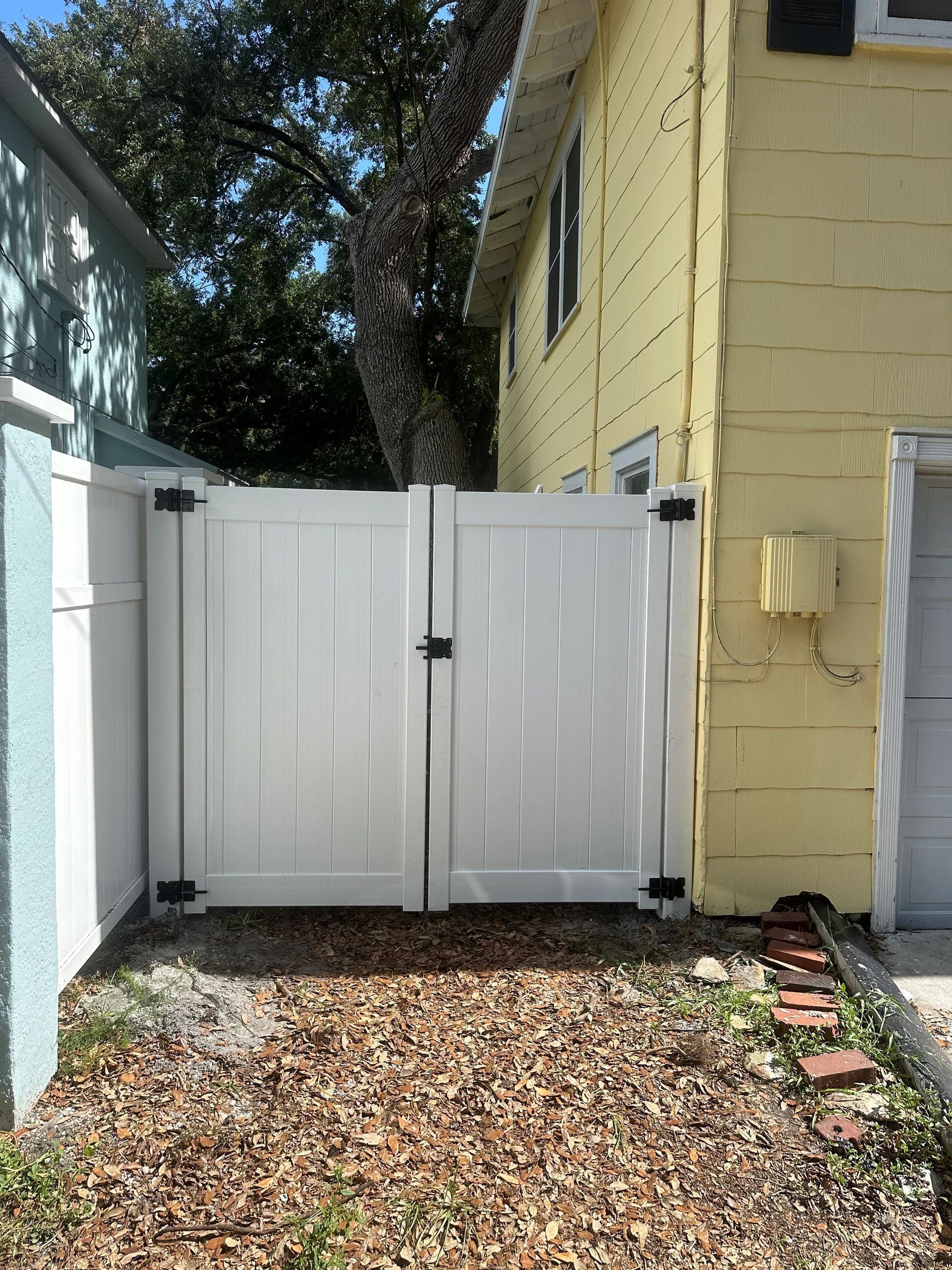 A white fence is sitting in front of a yellow house.
