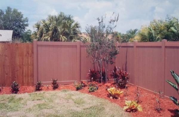 A backyard with a wooden fence and red mulch