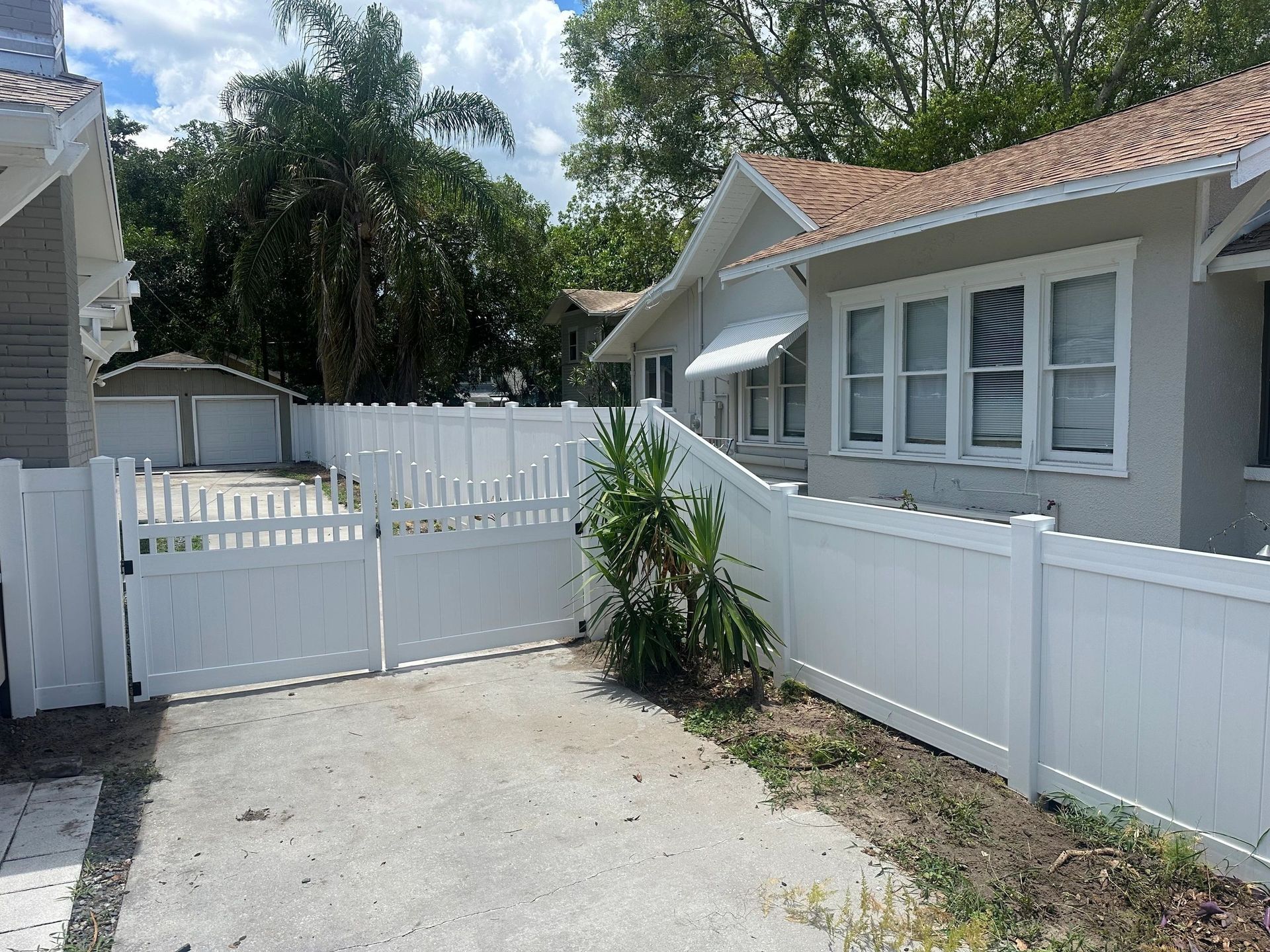 A white fence surrounds a driveway leading to a house