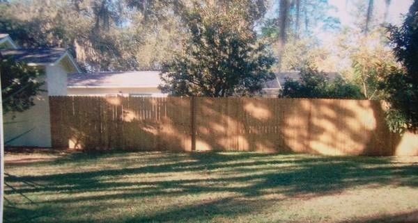 A wooden fence surrounds a lush green yard in front of a house.