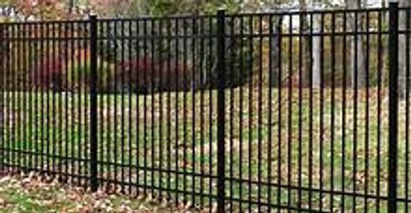 A black metal fence surrounds a lush green field.