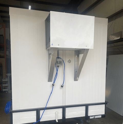 White industrial wall-mounted unit with blue hose and metal brackets in a warehouse-like room