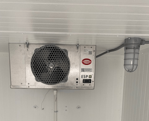 Wall-mounted metal ventilation unit with a circular fan and ducting on a white ceiling.