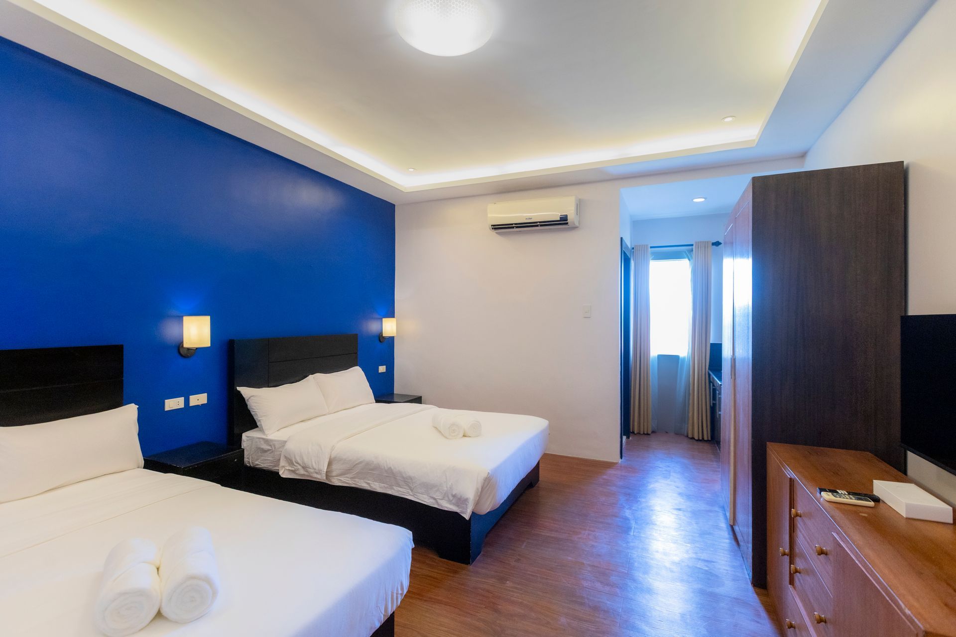 Bedroom with two beds, blue accent wall, wooden furniture, and doorway leading outside.