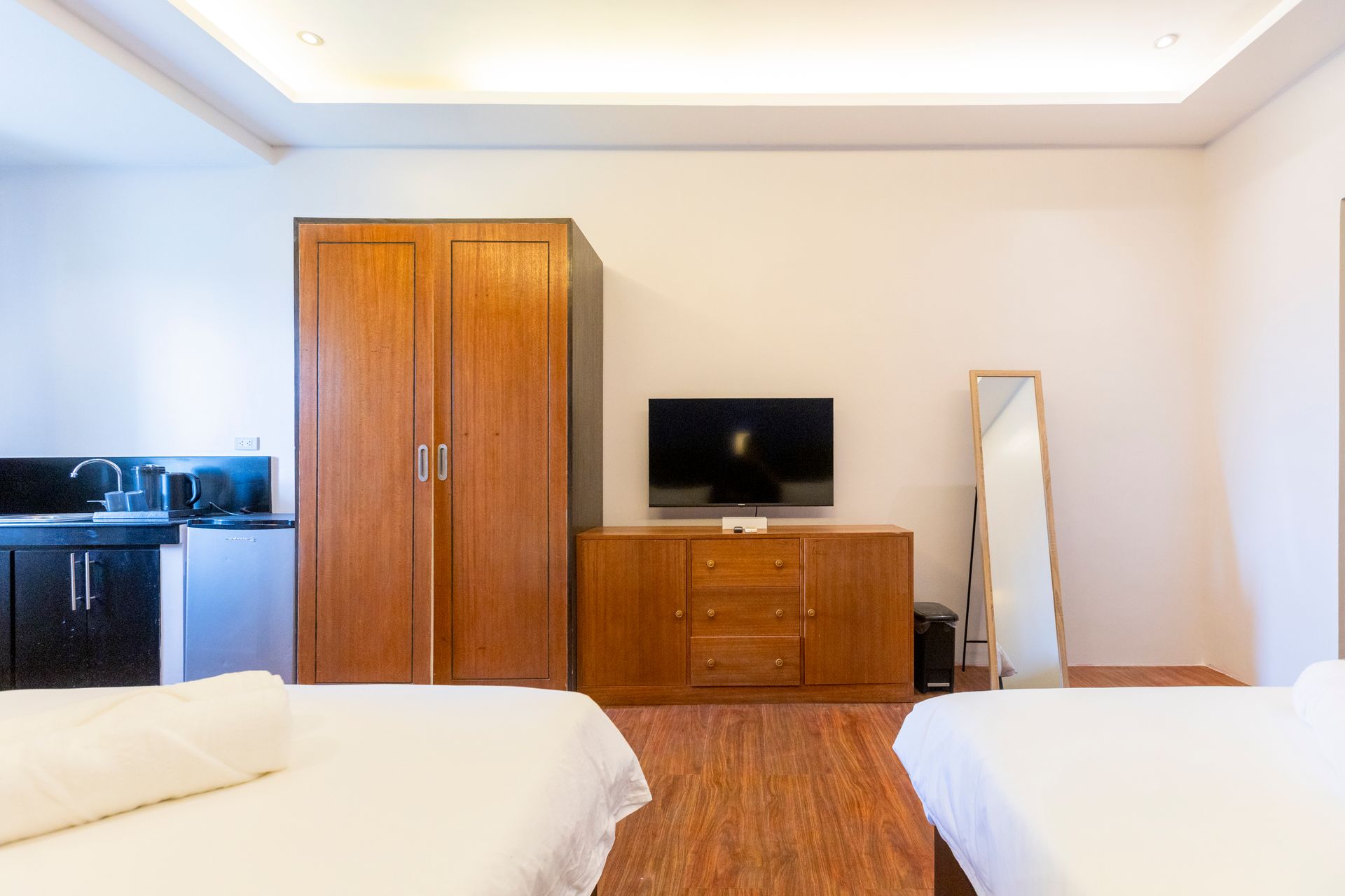 Studio apartment interior with a wardrobe, TV, mirror, and two beds.