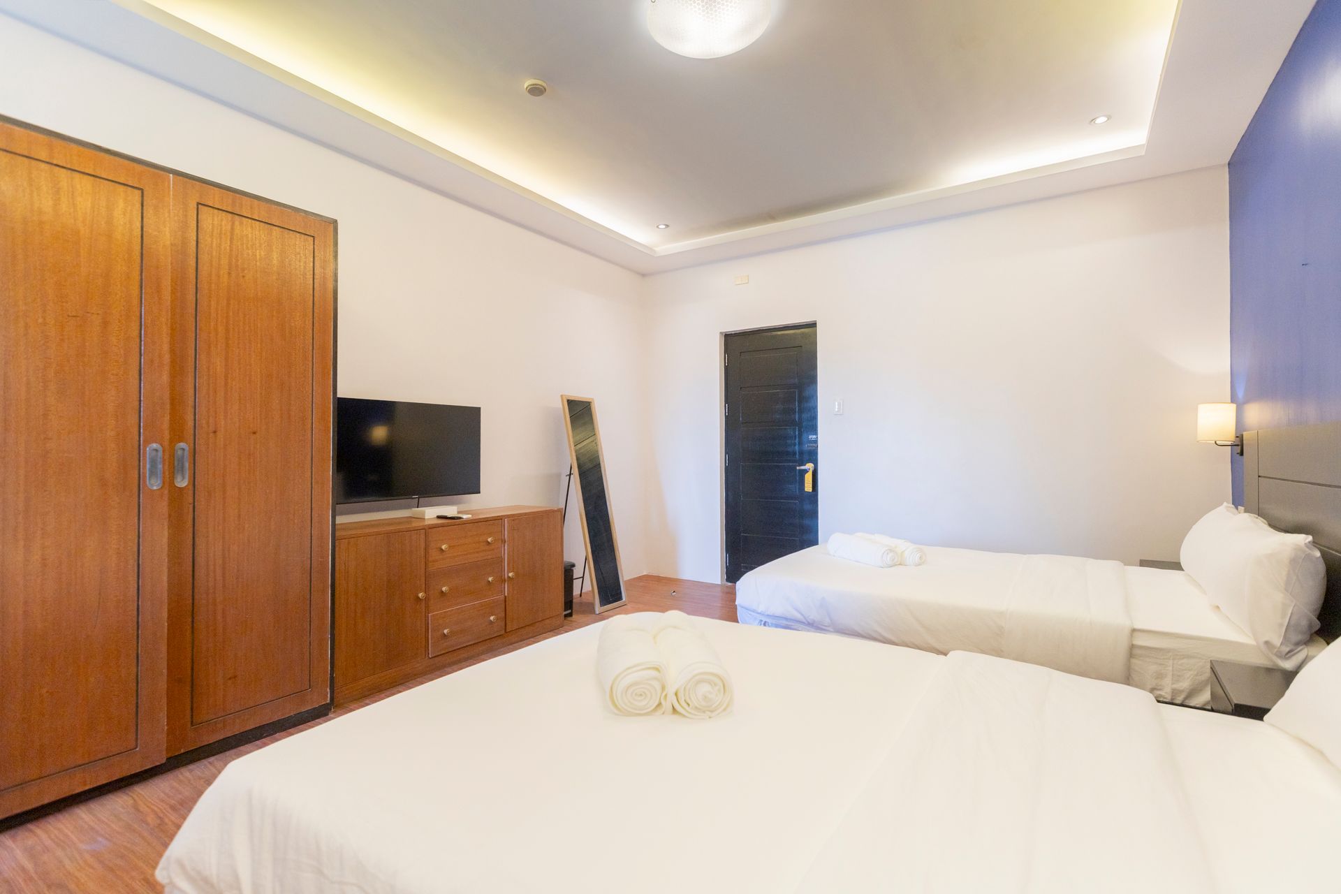 Bedroom with two beds, wooden wardrobe, TV, and blue accent wall.