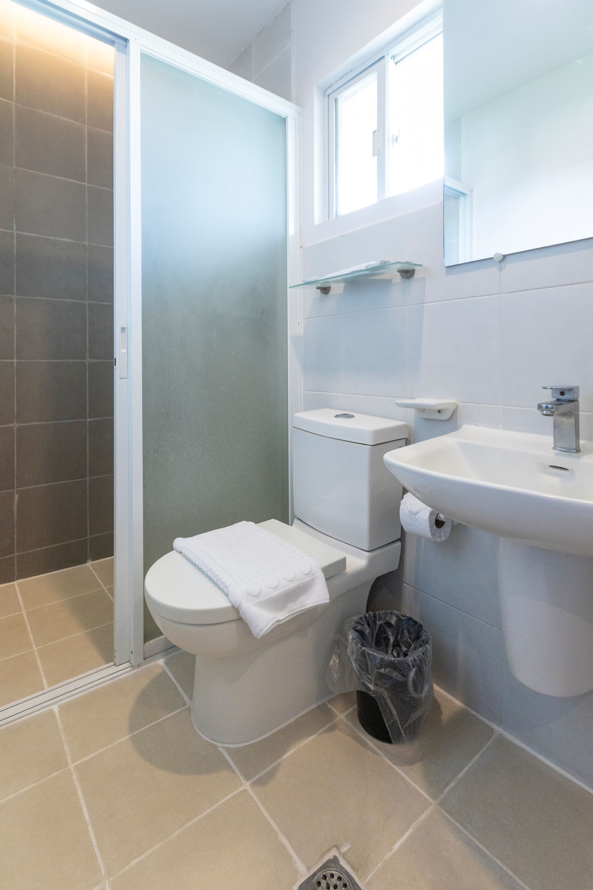 Bathroom with a toilet, sink, and shower. The walls are tiled in shades of gray.