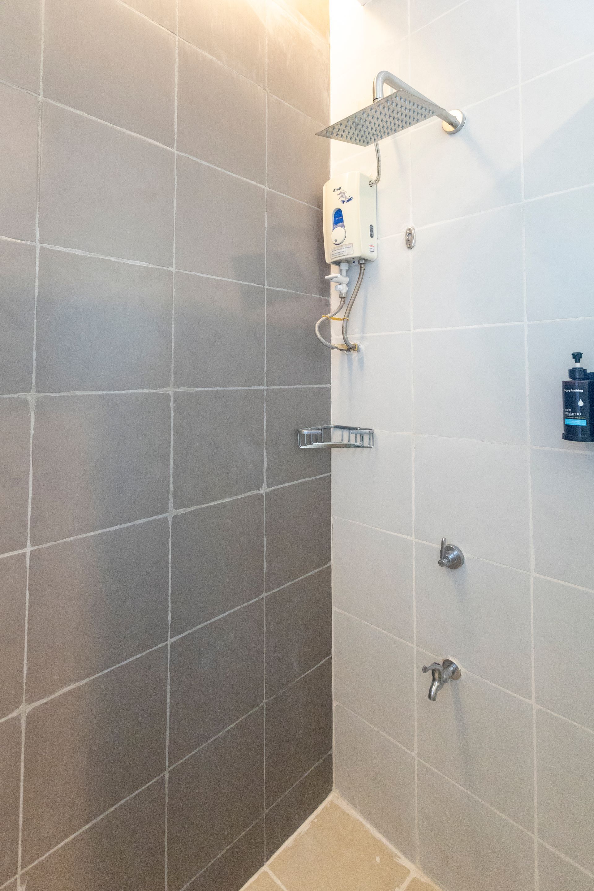 A tiled shower with a square showerhead, water heater, and soap dispensers.