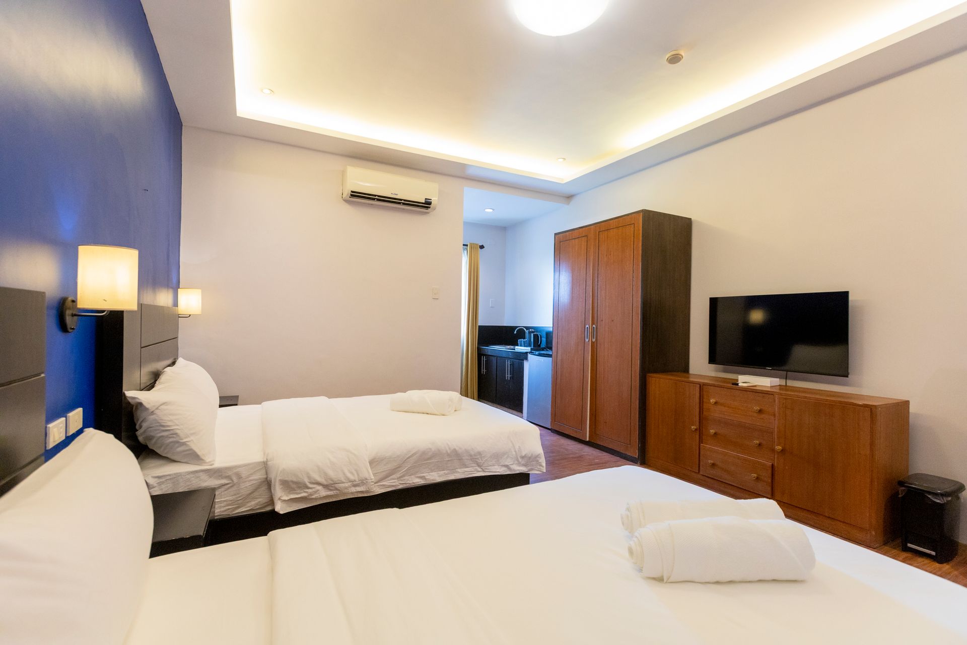 Hotel room with two beds, TV, wooden furniture, and air conditioning unit.