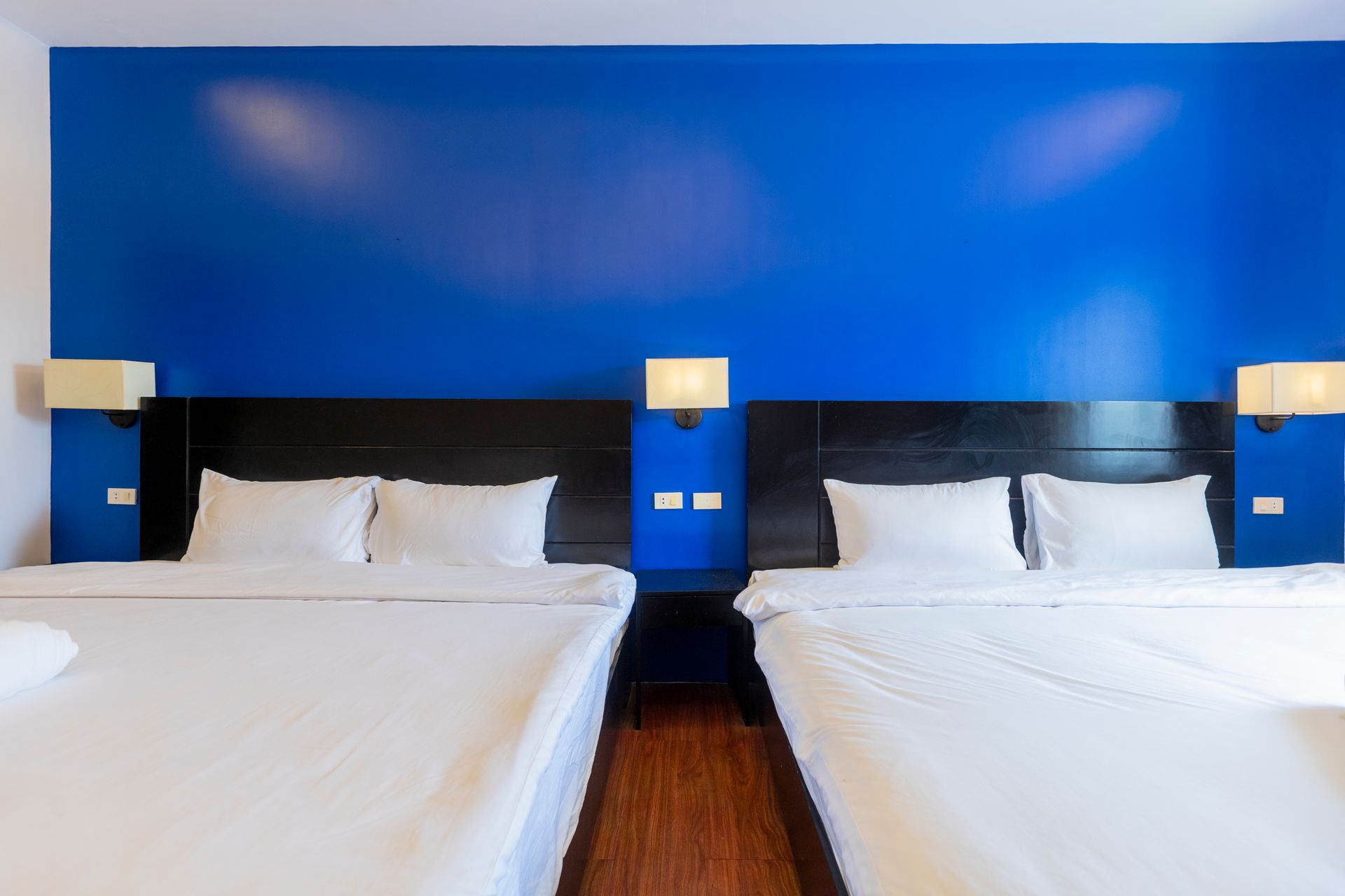Two queen beds in a room with blue wall, black headboards, and sconce lighting.
