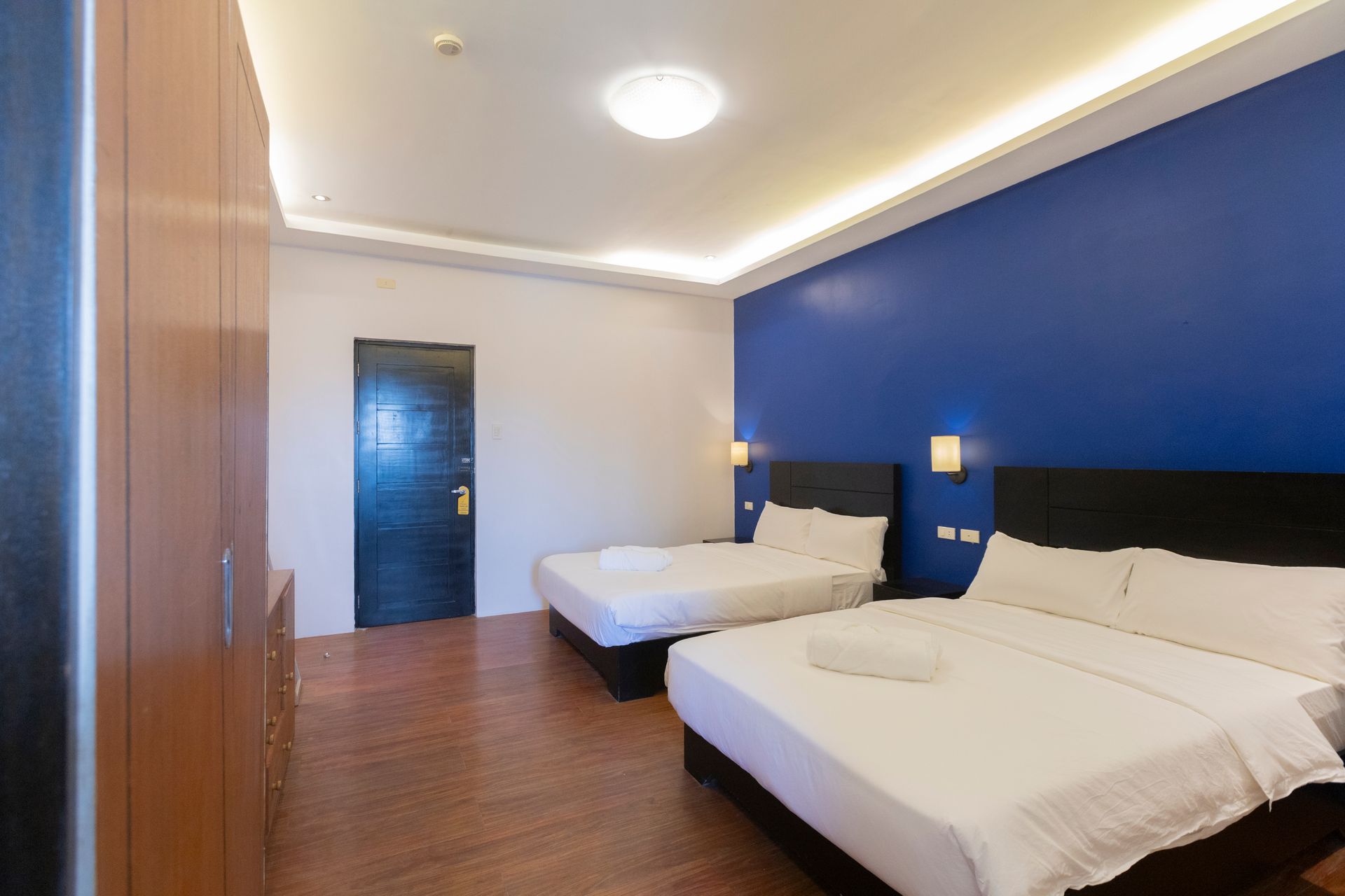 Hotel room with two beds, blue accent wall, wooden floor, and a closet.
