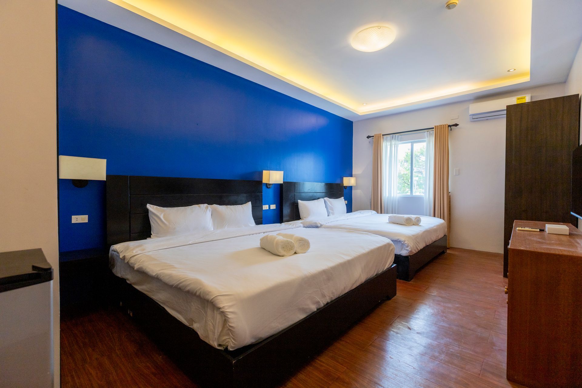 Hotel room with two beds, blue accent wall, wooden floor, and a closet.