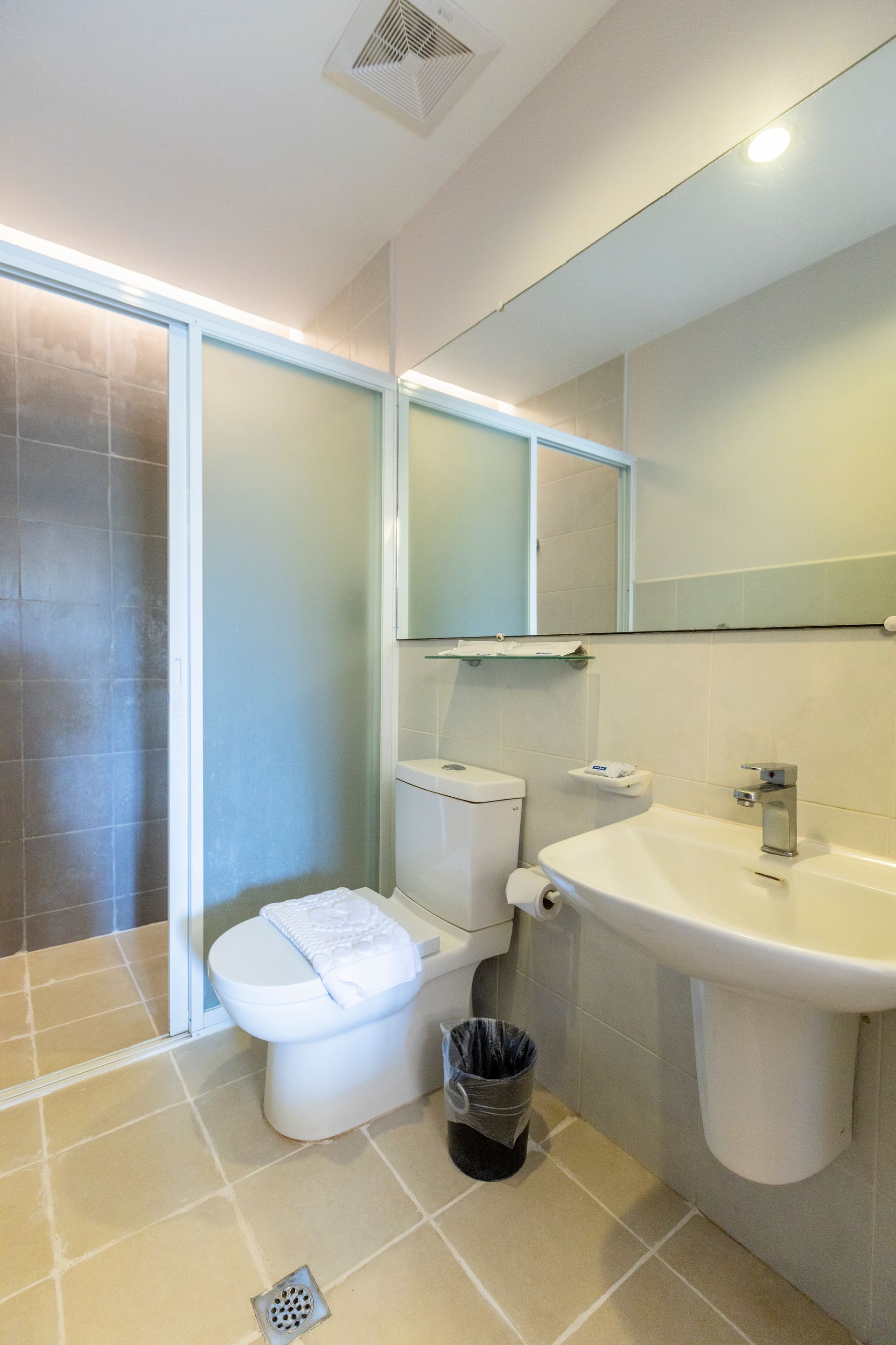 Bathroom with a white toilet, sink, and glass shower door; gray tile floor and walls.