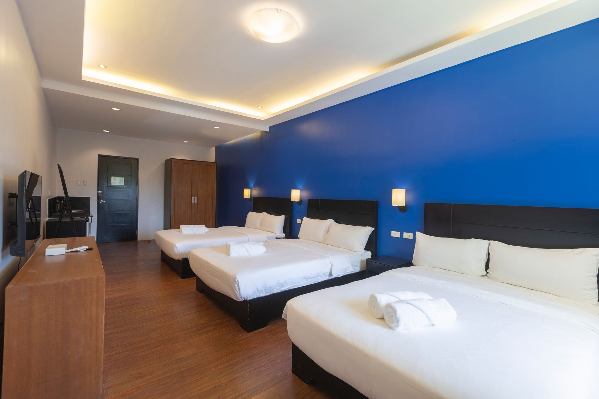 Hotel room with three queen beds, blue accent wall, and wood floors.