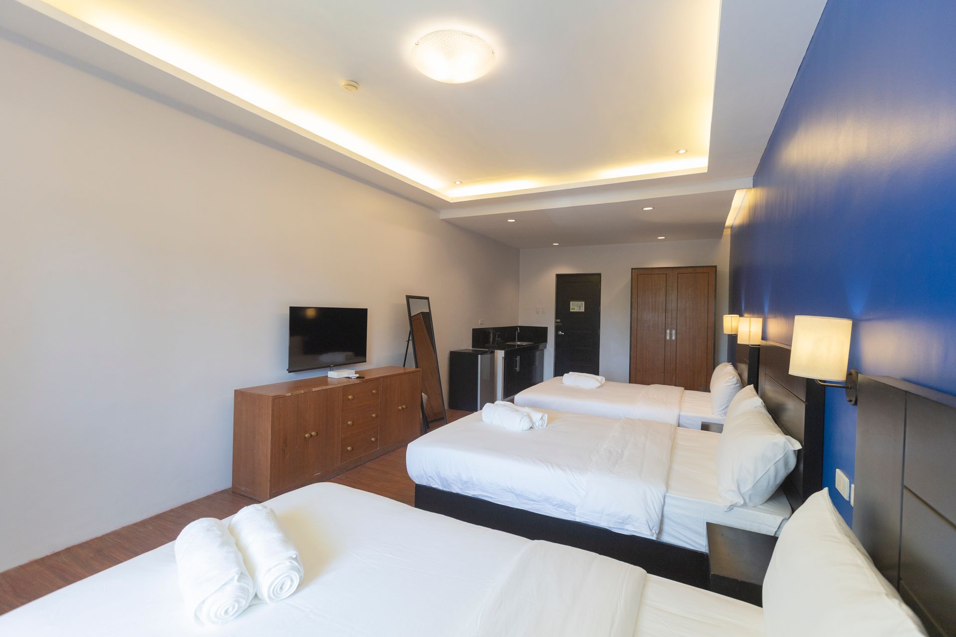 Hotel room with three beds, a TV, and a blue accent wall.